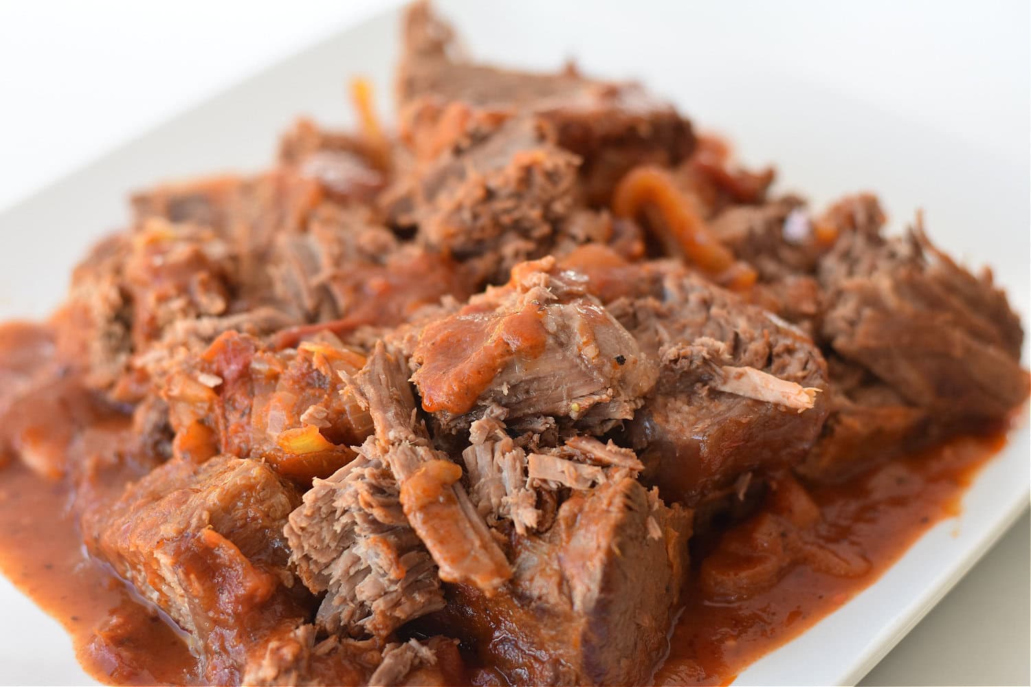 Beef bottom roast recipes cooked to perfection in a savory tomato based Italian sauce on a white plate. 