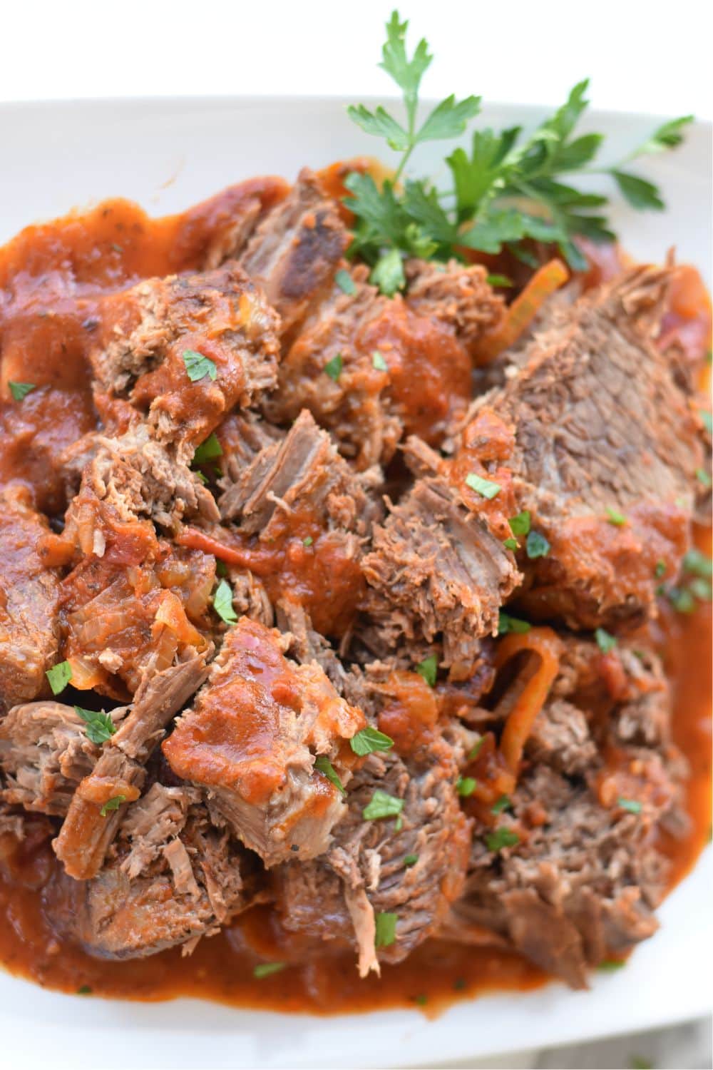 Cut up beef bottom round roast with a tomato sauce on a white plate. 