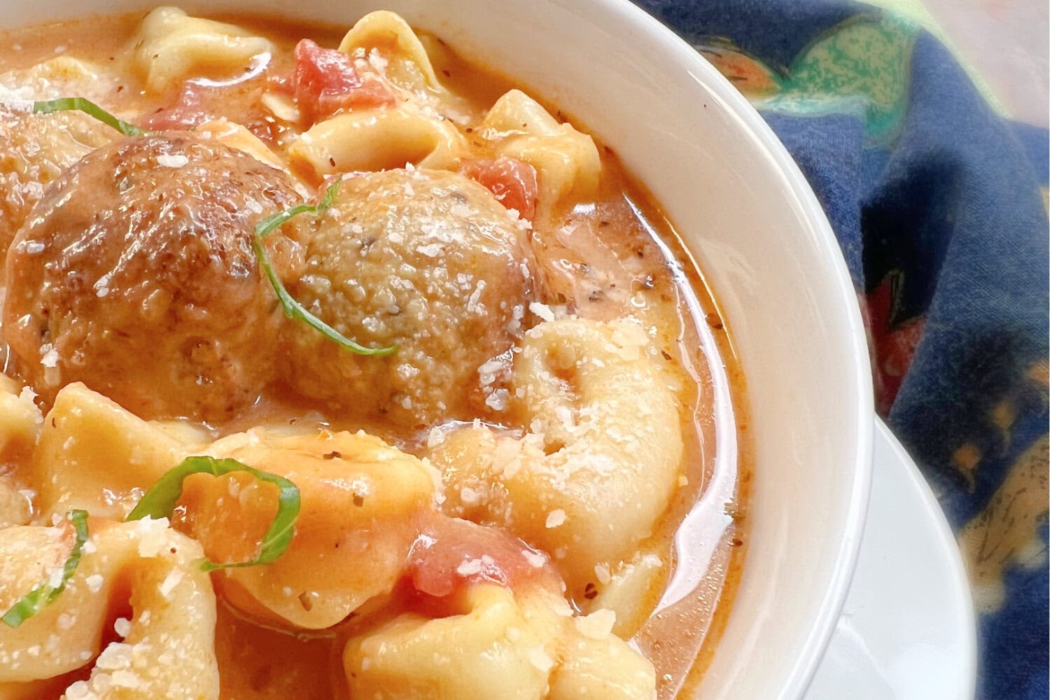 A white bowl of meatball soup with tortellini.