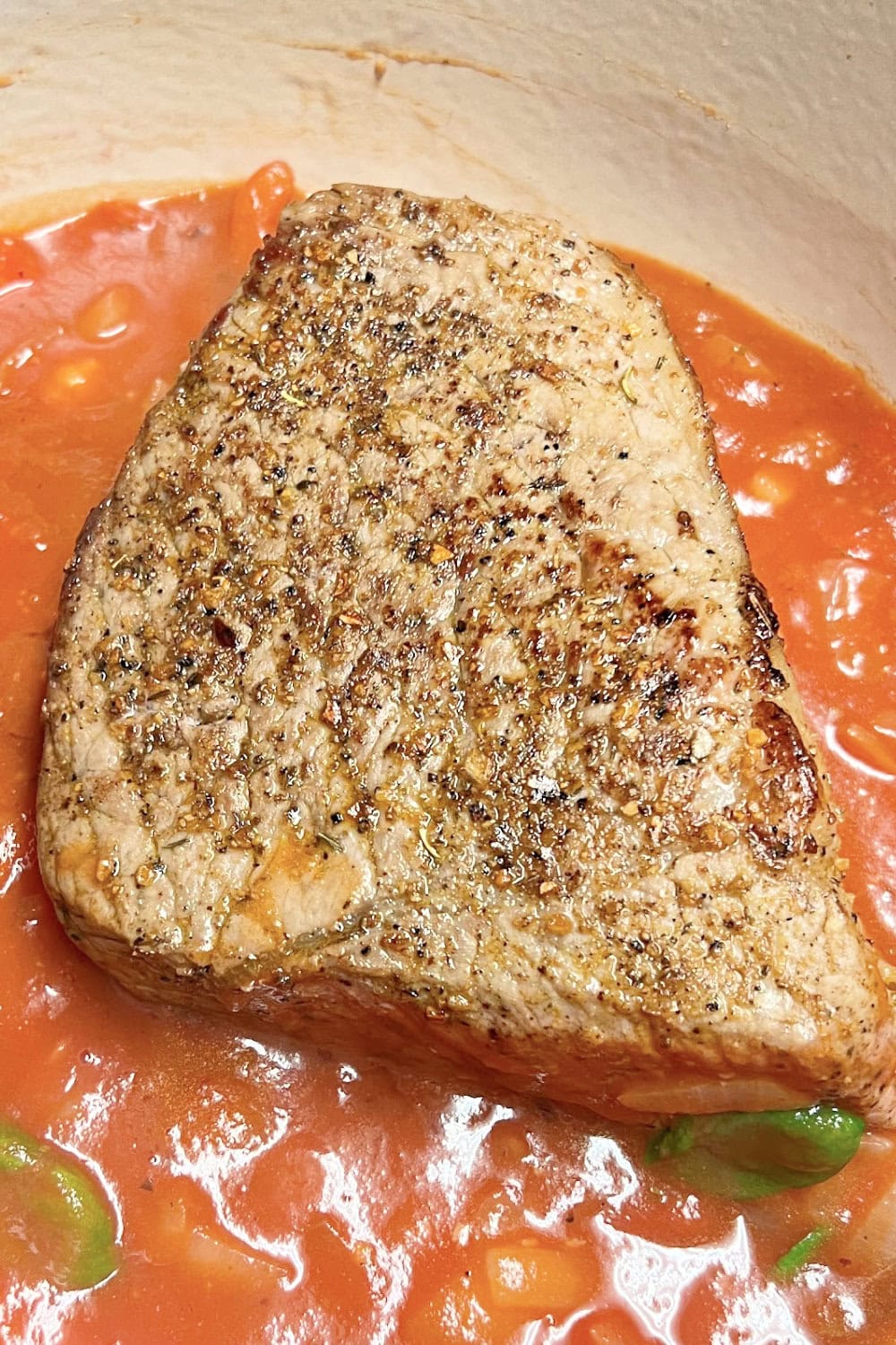 Seared bottom round roast in tomato sauce in a Dutch oven. 