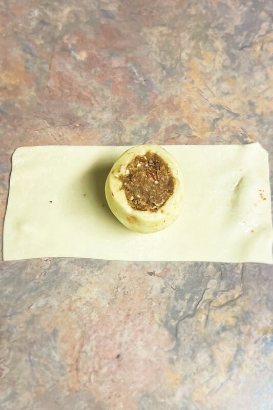 A cut piece of pillsbury pie crust dough with a filled apple. 