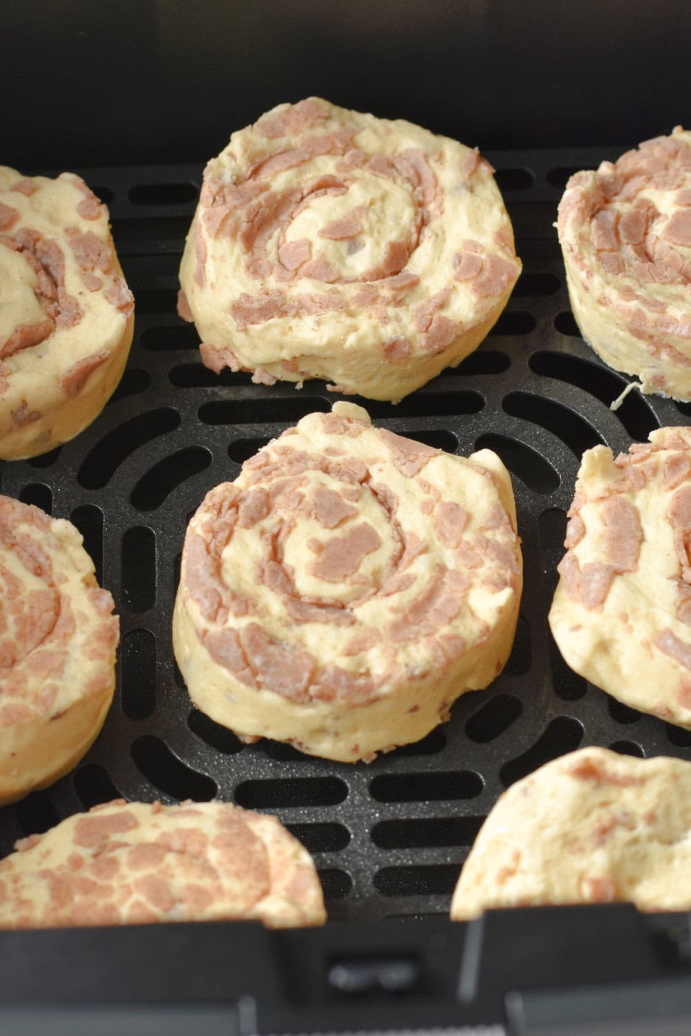 Cinnamon rolls placed onto the air fryer basket in preparation to cook. 