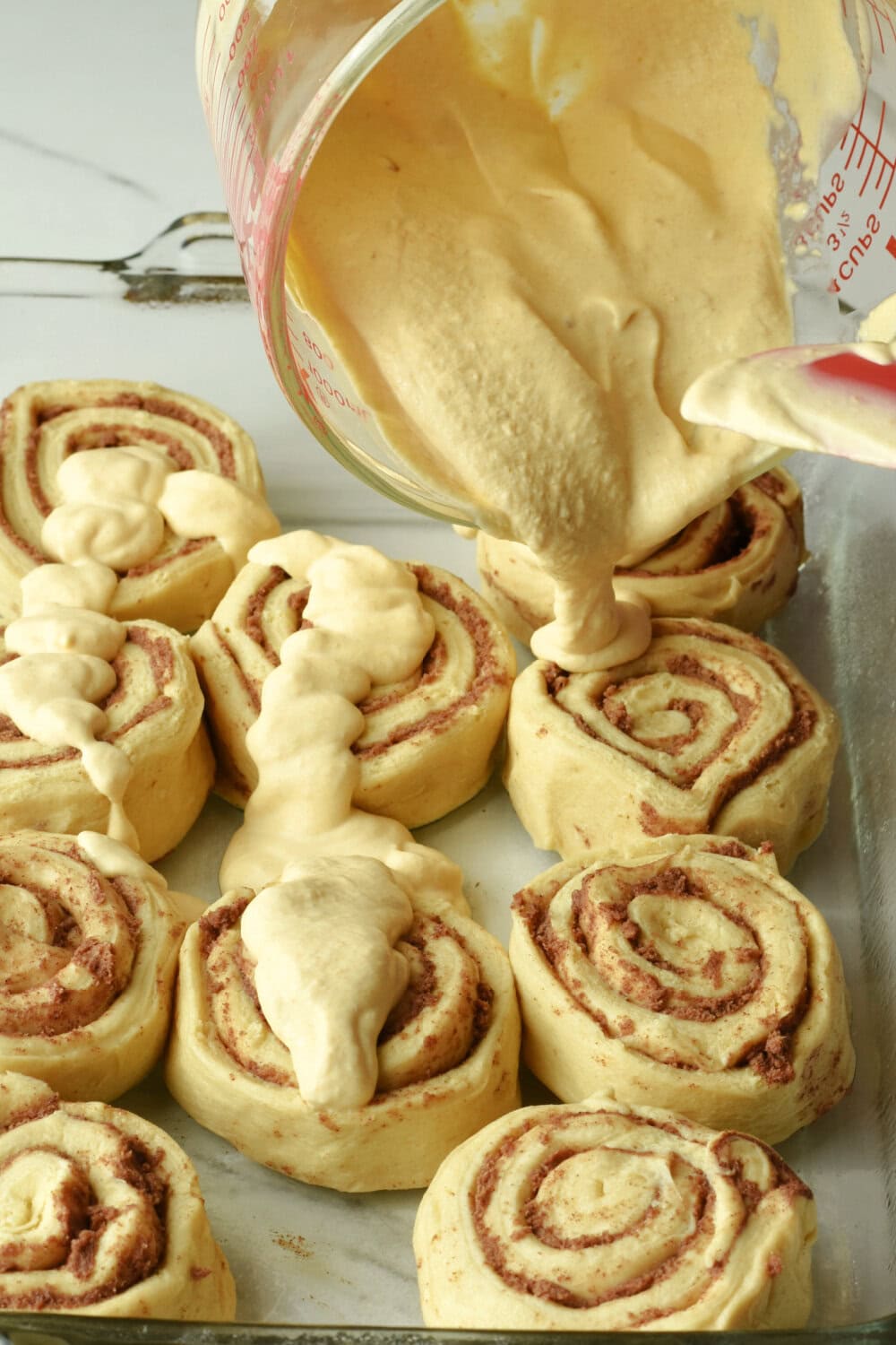 Pouring pumpkin whipping cream over the cinnamon rolls. 