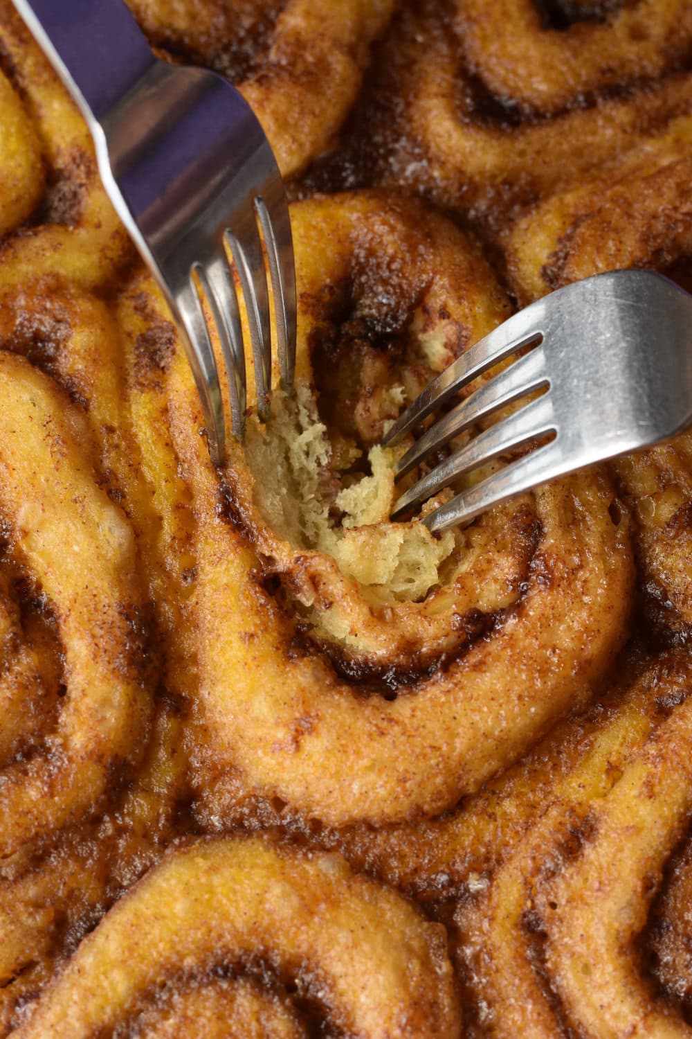 Checking a cinnamon roll for doneness at the center using two forks. 