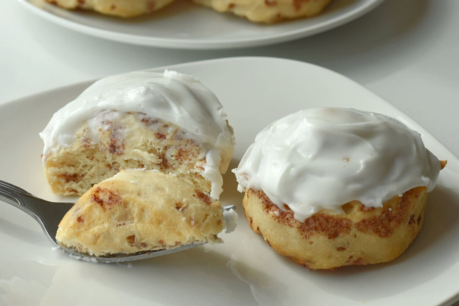 Pillsbury cinnamon rolls made in the air fryer with frosting on a white plate with a fork. 