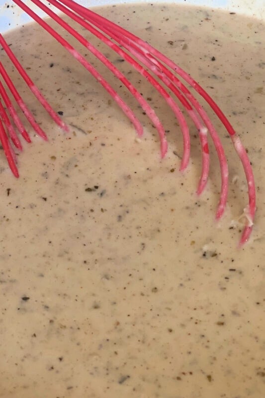 Fully thickened cream sauce with a red whisk in the skillet. 