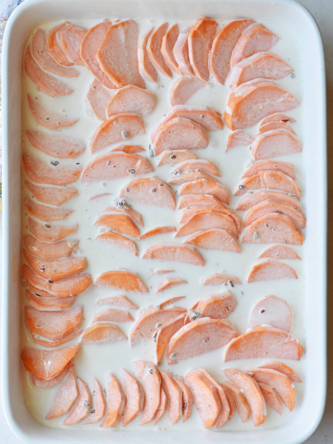 scalloped-sweet-potatoes-in-sauce Sliced potatoes with cream sauce on top.