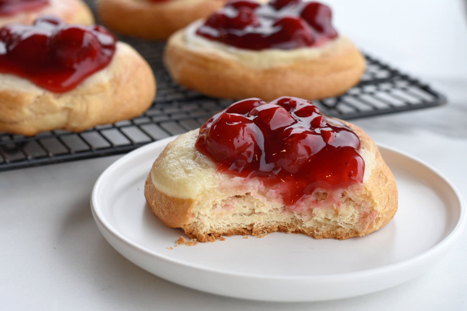 Cherry cheesecake Danish made from pillsbury crescent dough, cherry pie filling and cream cheese on a white plate. 