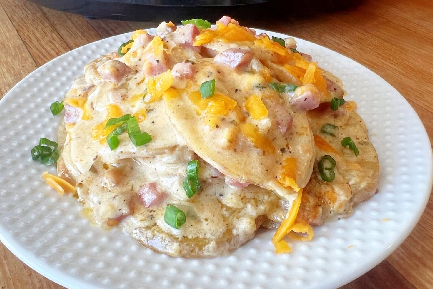 A hot and fresh serving of Scalloped Potatoes and Ham on a white plate. 