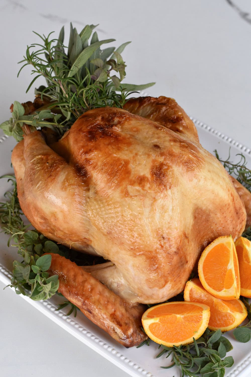 A crispy whole turkey made in an electric roaster oven stuffed with fresh herbs and surrounded by oranges. 