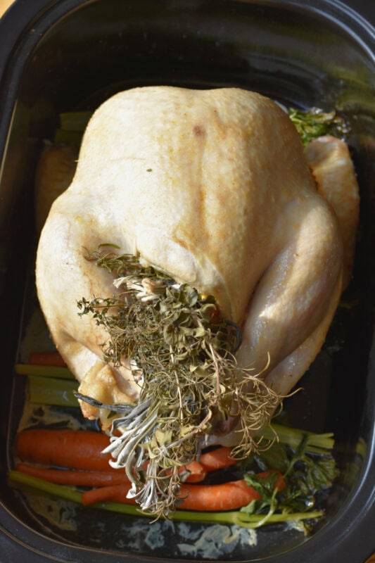 A partially cooked whole turkey in a roaster with cooked herbs. 