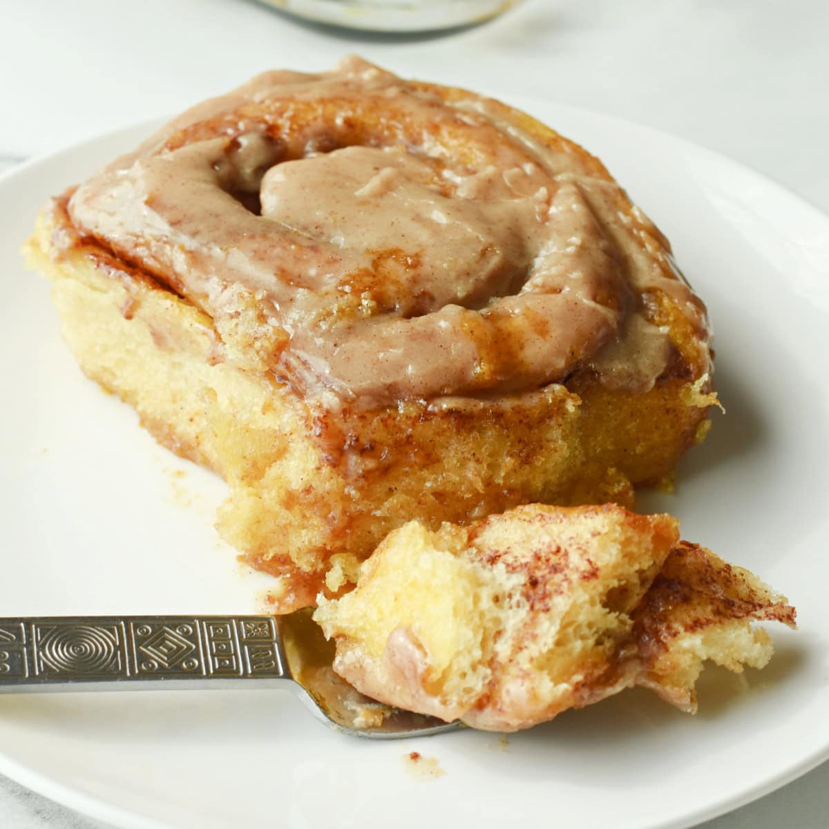 A pumpkin cinnamon roll on a white plate with a bite on a fork.