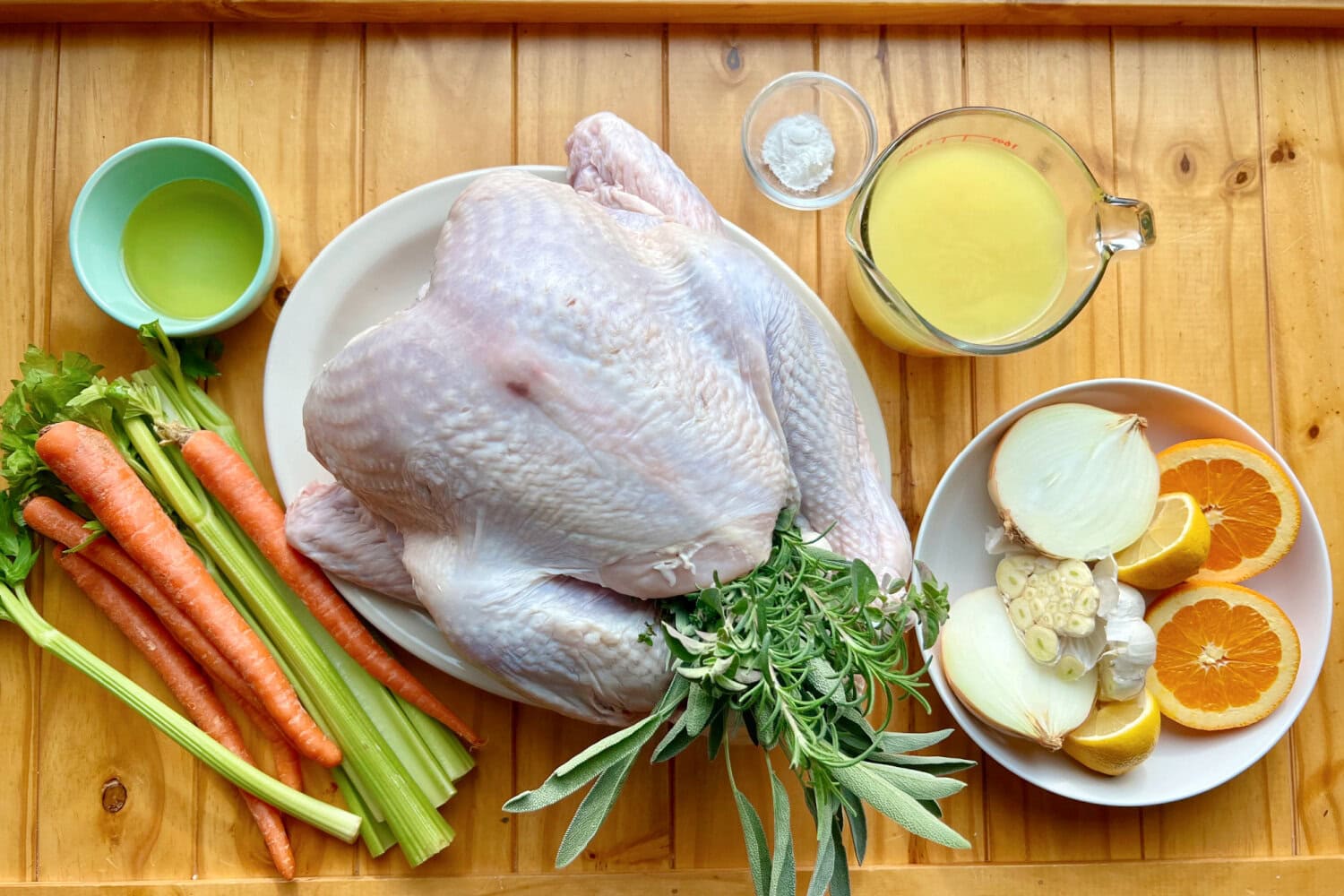 Ingredients to make turkey in an electric roaster that include carrots, celery, herbs, broth, garlic, onions, oil, and oranges. 