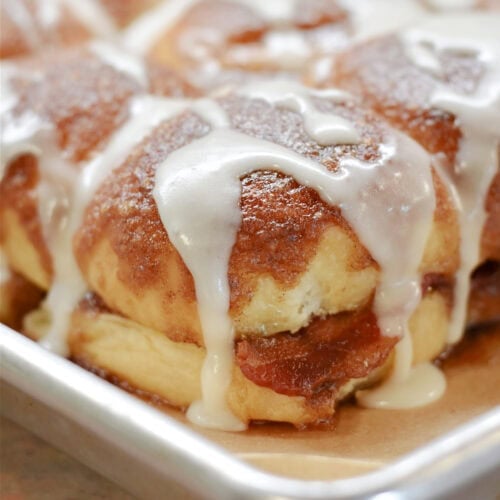 Bacon and cinnamon rolls in a hawaiian roll with icing on a serving plate.