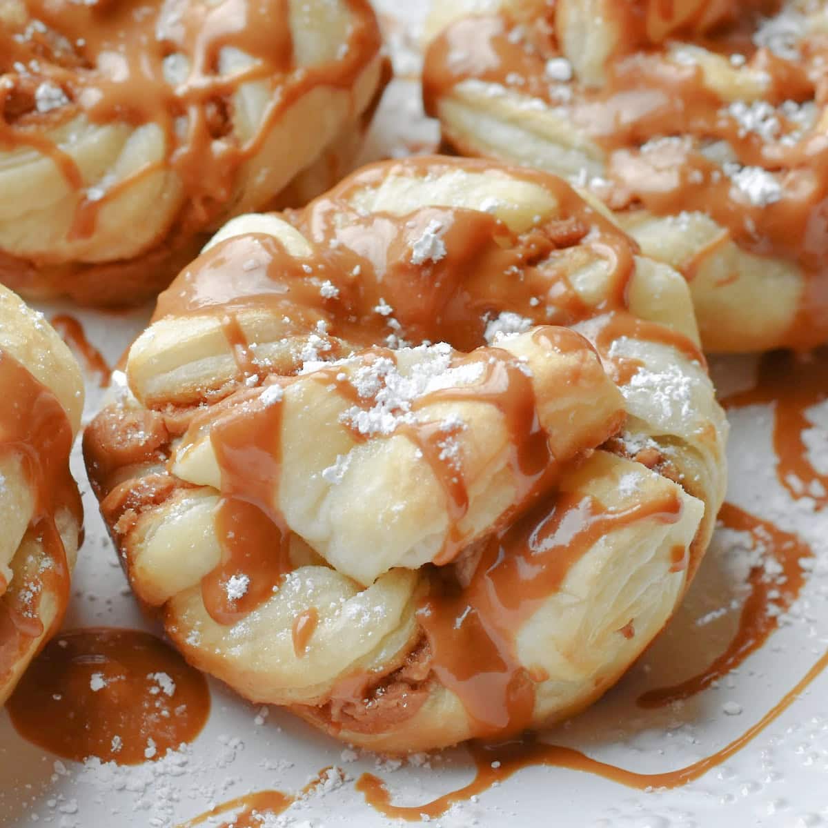 Goey biscoff cinnamon rolls frosted with powdered sugar on a white plate.