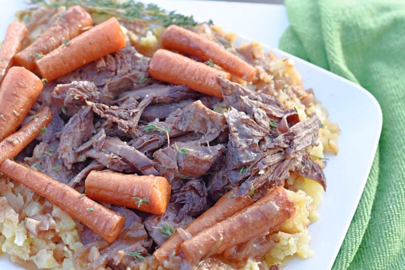 Braised chuck roast with carrots and potatoes on a white plate. 