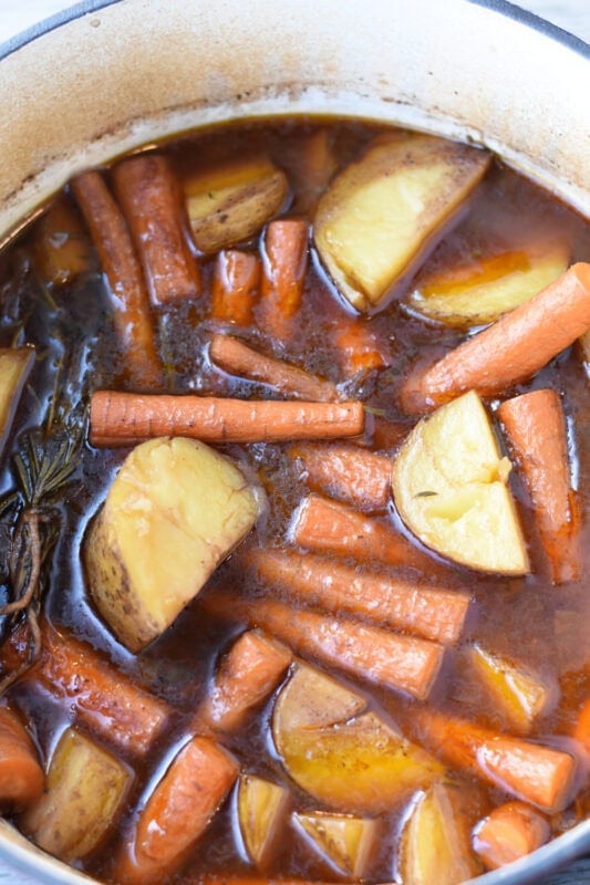 Braised chuck roast with potatoes and carrots in the dutch oven with broth. 