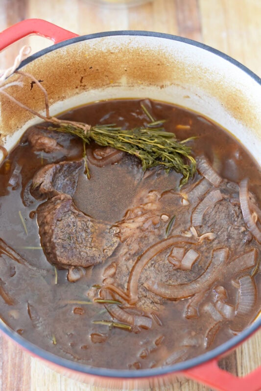 Partially braised beef in seasoned broth in a dutch oven. 