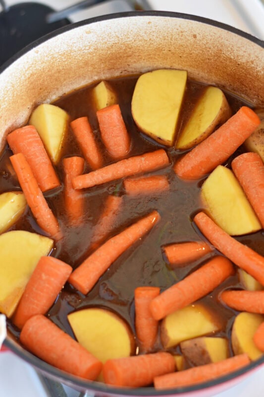 Beef with beef broth, carrots and potatoes in a dutch oven. 