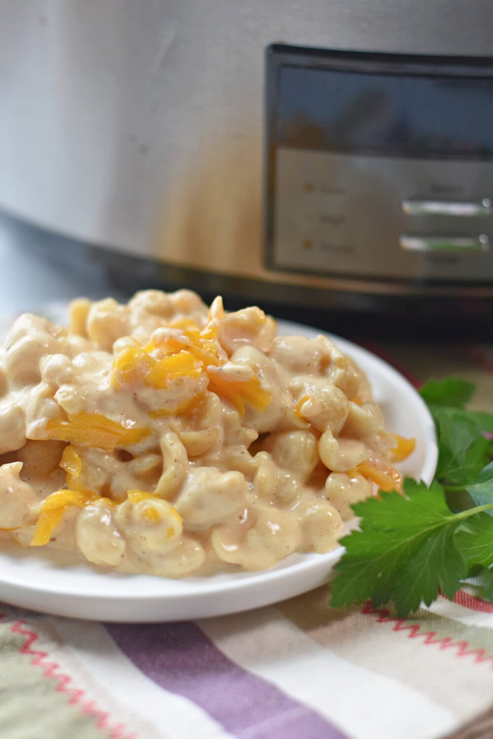 crock-pot-mac-cheese Crockpot Velveeta Mac and Cheese on a white serving plate with a slow cooker behind it.