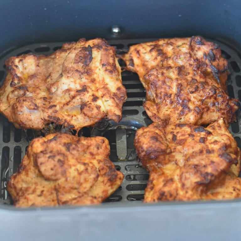 Skinless boneless chicken thighs in a air fryer basket fully cooked.