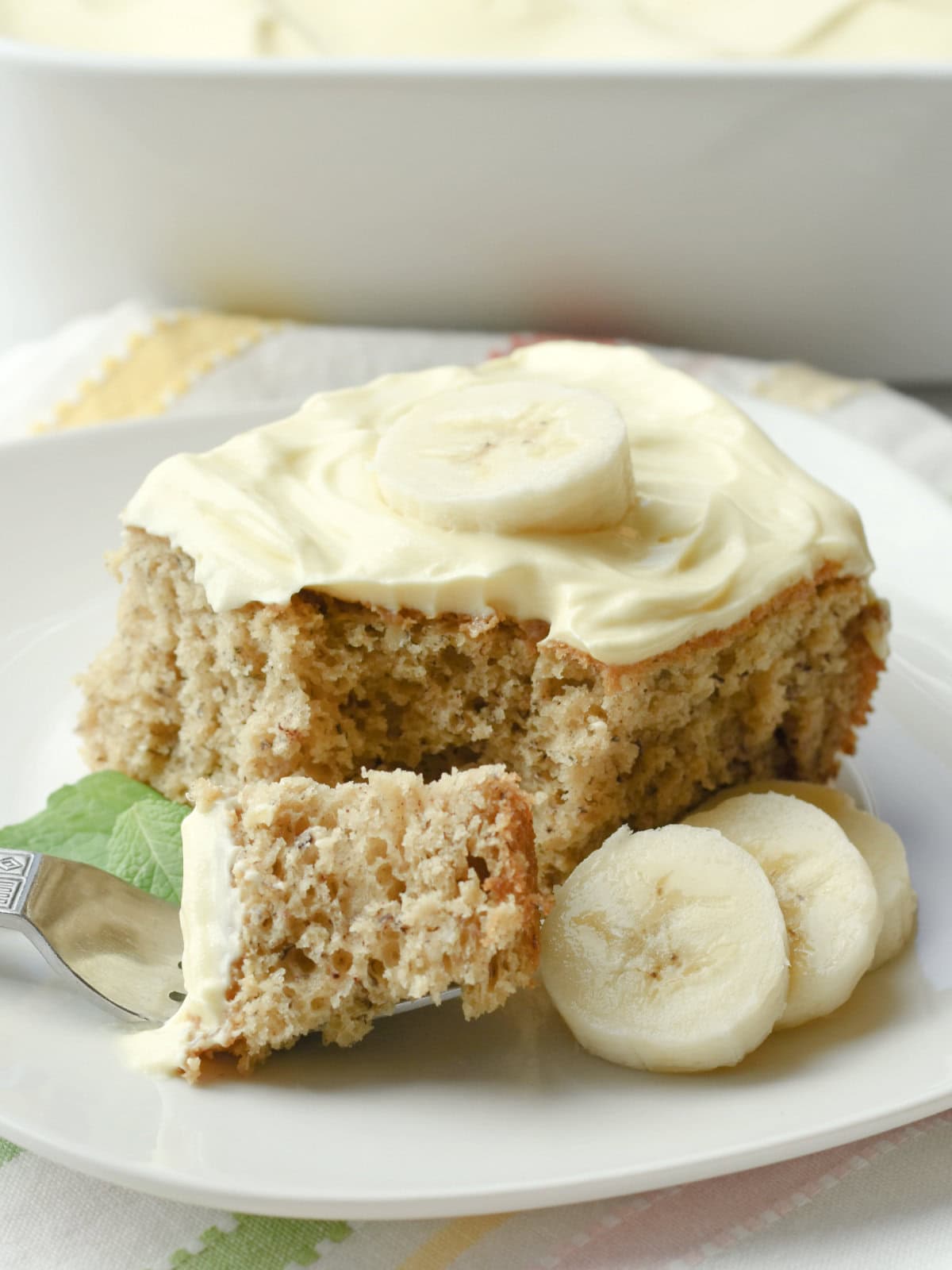 Banana cake using cake mix cut into a bitesized piece with a fork and bananas on top. 