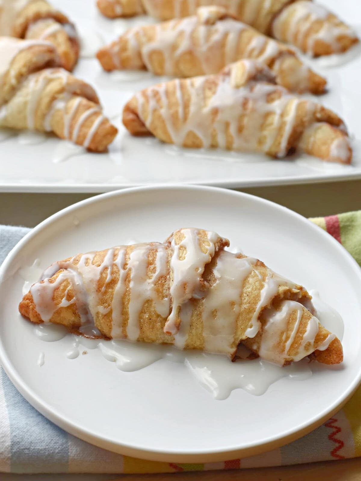 Crescent Roll Cinnamon Rolls with easy icing on a white plate with other rolls behind it. 