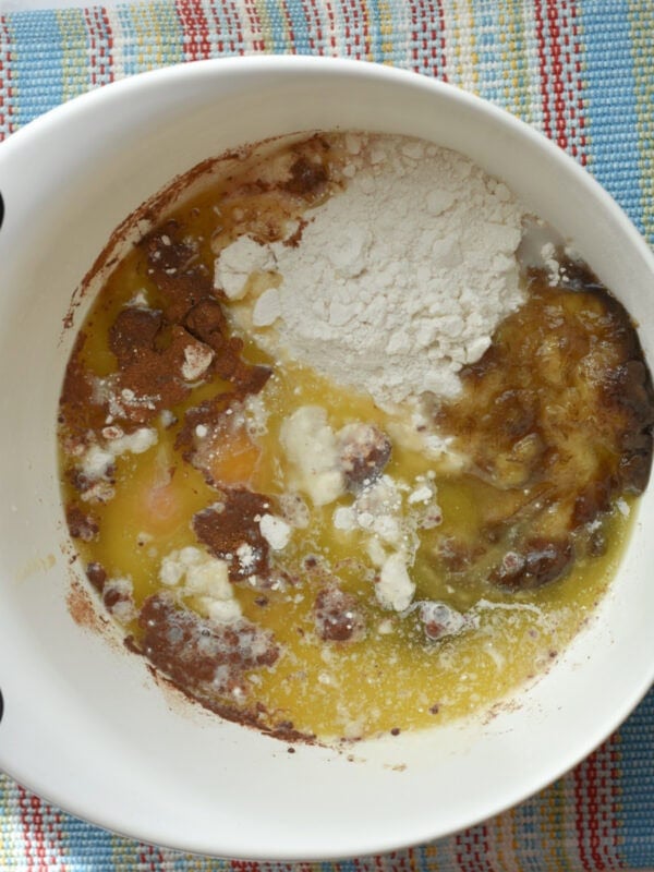 Flour mixture, ripened bananas, milk, and eggs in a white mixing bowl. 