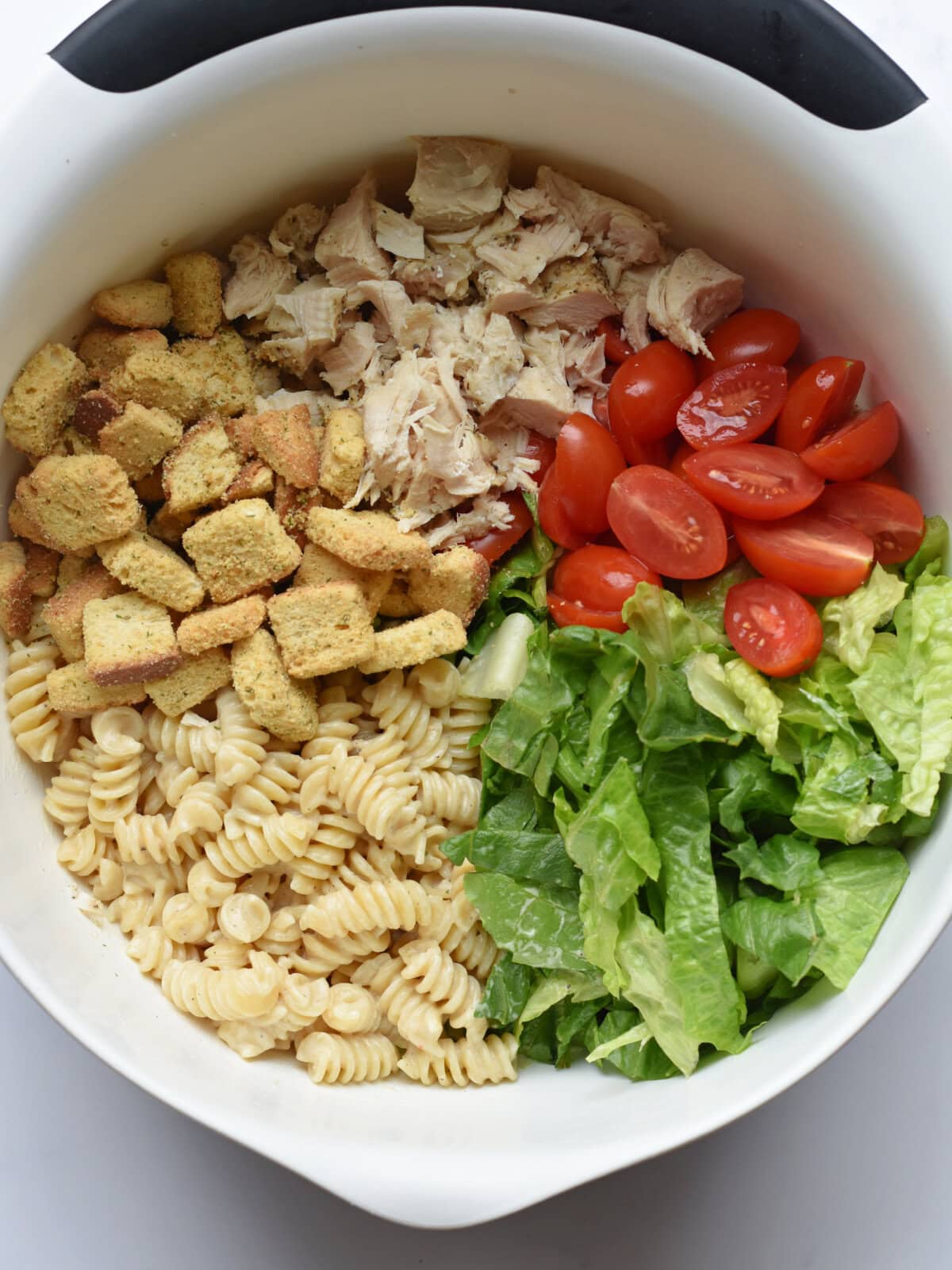 caesar-salad-pasta-unmixed A mixing bowl with chicken, romaine lettuce, croutons, marinated Rontini noodles and tomatoes.