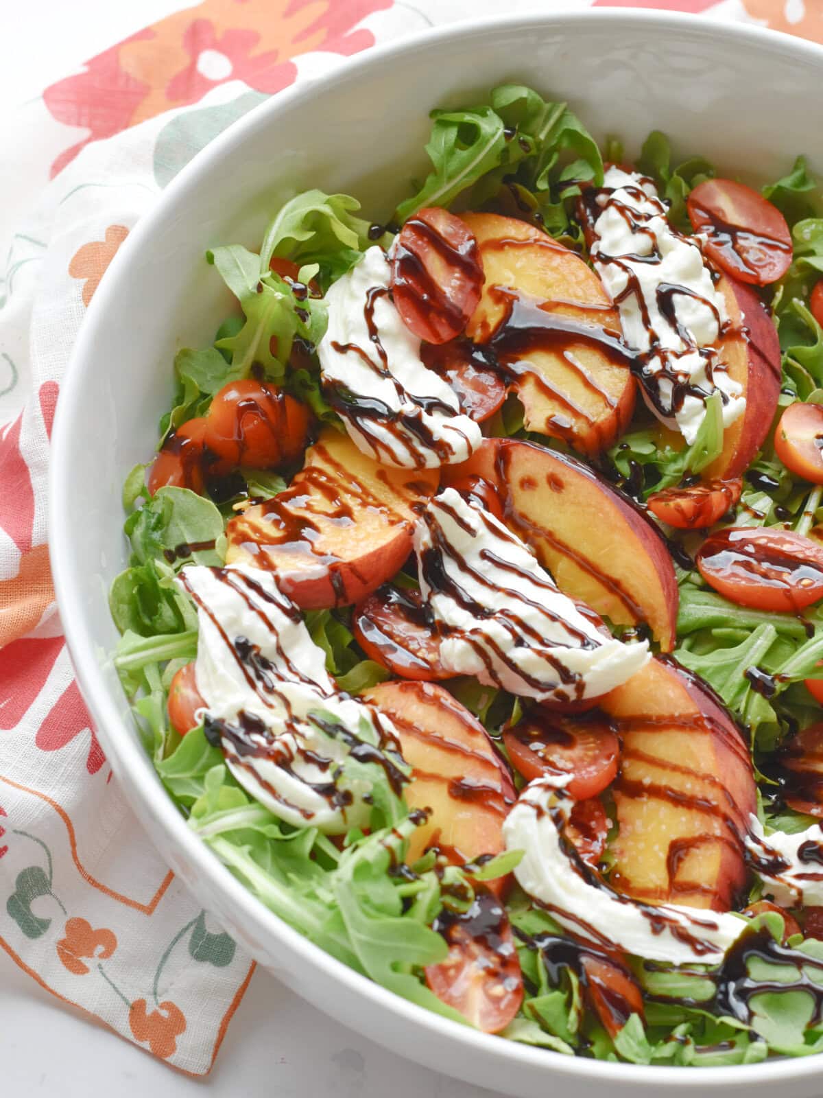 peach-burrata-salad-serving Peach Burrata Salad with Arugula in a serving bowl with balsamic glaze drizzled on top.