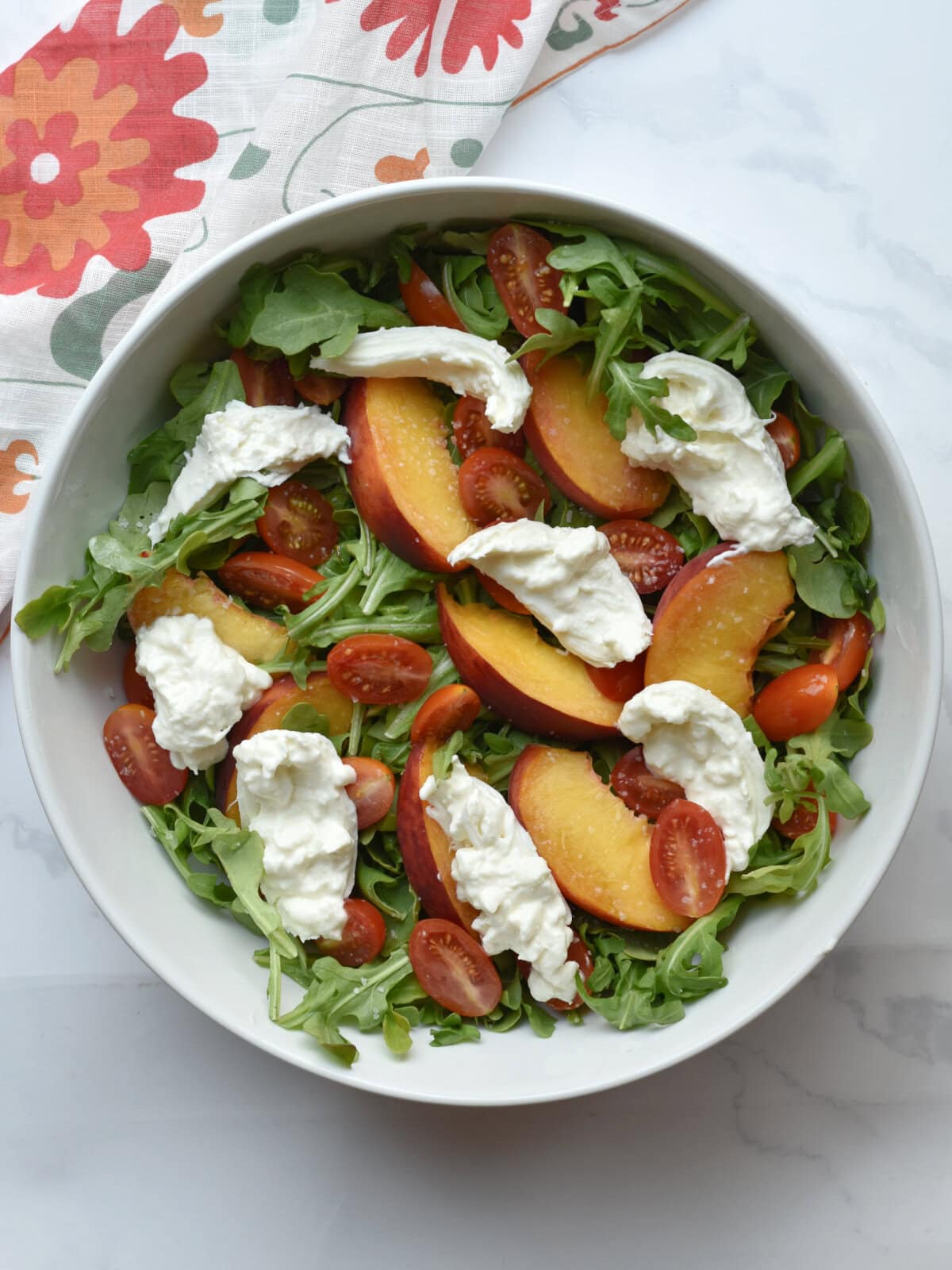 Burrata-cheese-pulled Burrata cheese pulled apart on the top of peach salad.