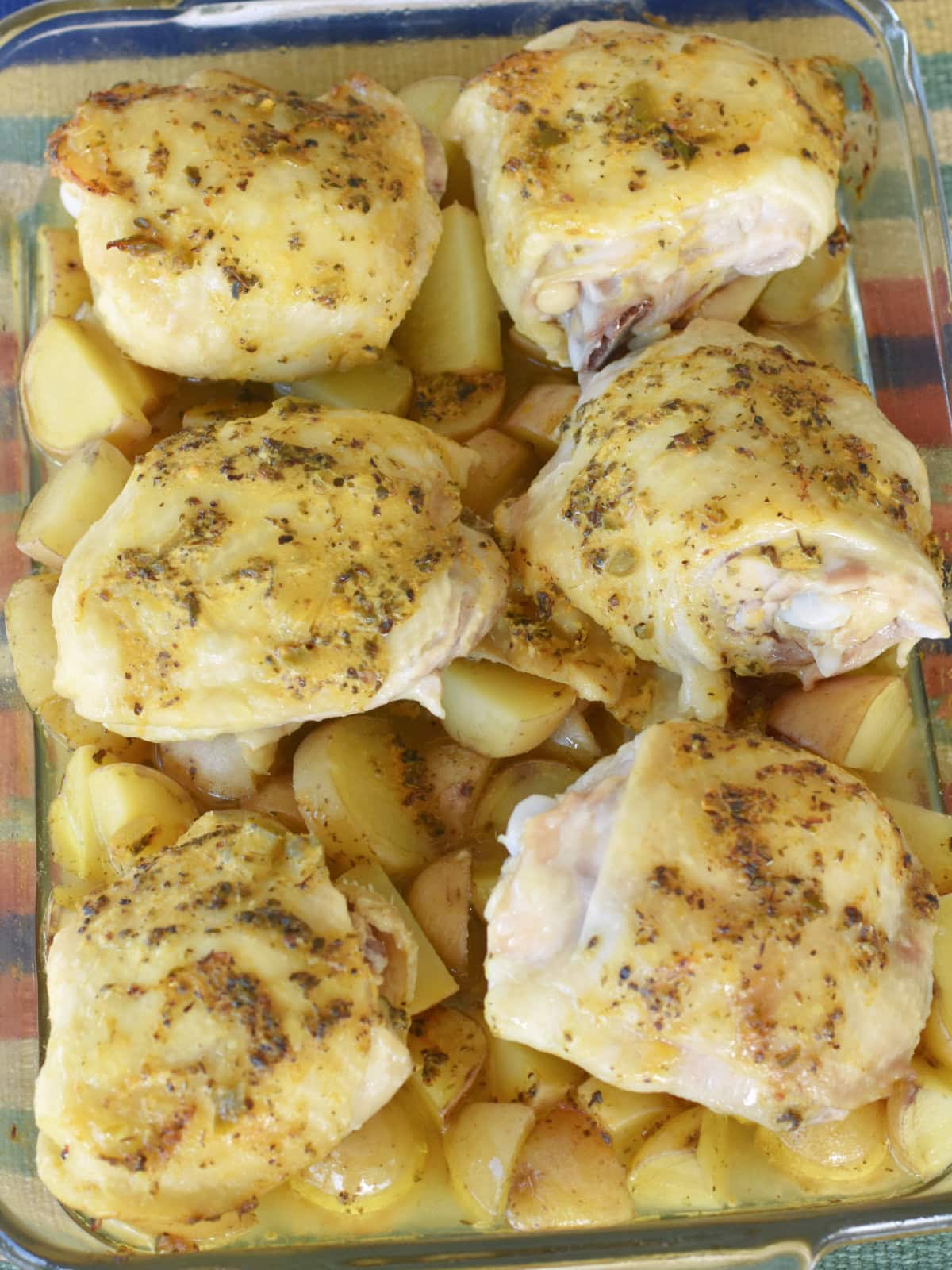 Chicken-thighs-potatoes-uncovered Partially cooked chicken thighs with potatoes.