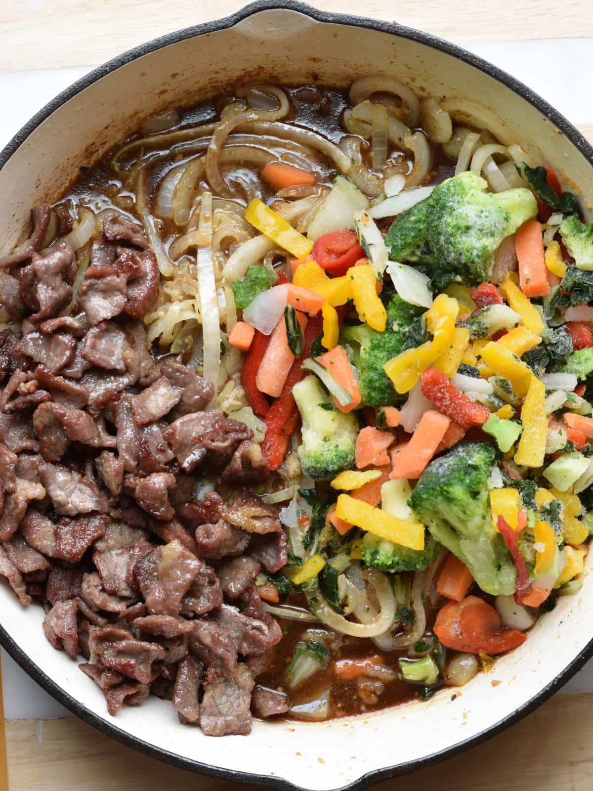 Uncooked beef bottom round steak stir fry in cast iron skillet. 