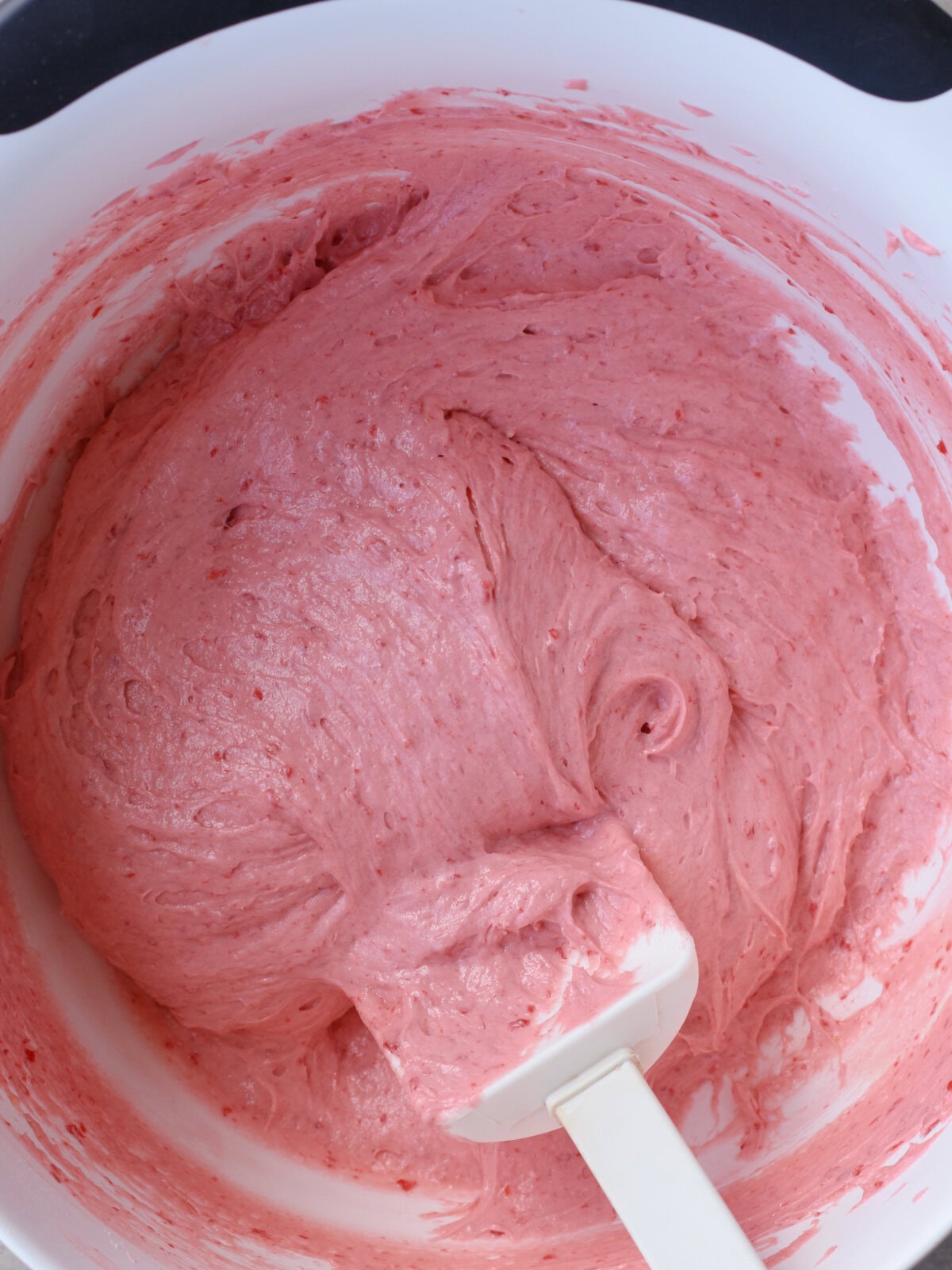 Pink cake batter in a white mixing bowl with a spatula. 