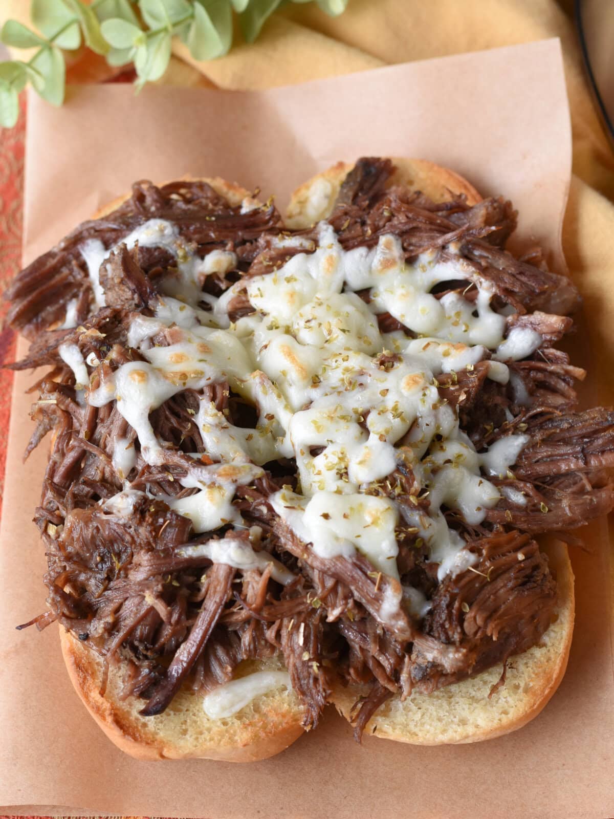 Pulled Beef Sandwiches in the Crock Pot ready to eat on butcher paper with melted cheese sprinkled on top. 