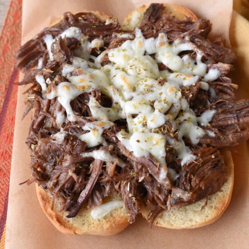 Slow cooker pulled beef sandwiches with shredded cheese.
