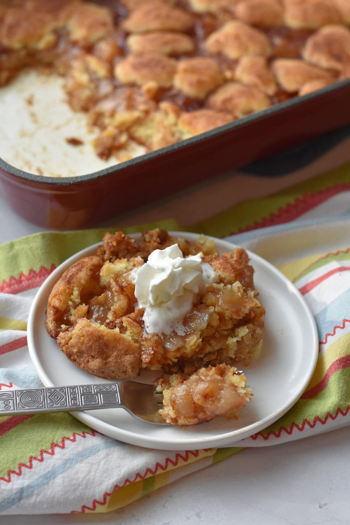 Snickerdoodle Cake made in dump cake style with a plated serving in the front of the picture and a pan in the background. 