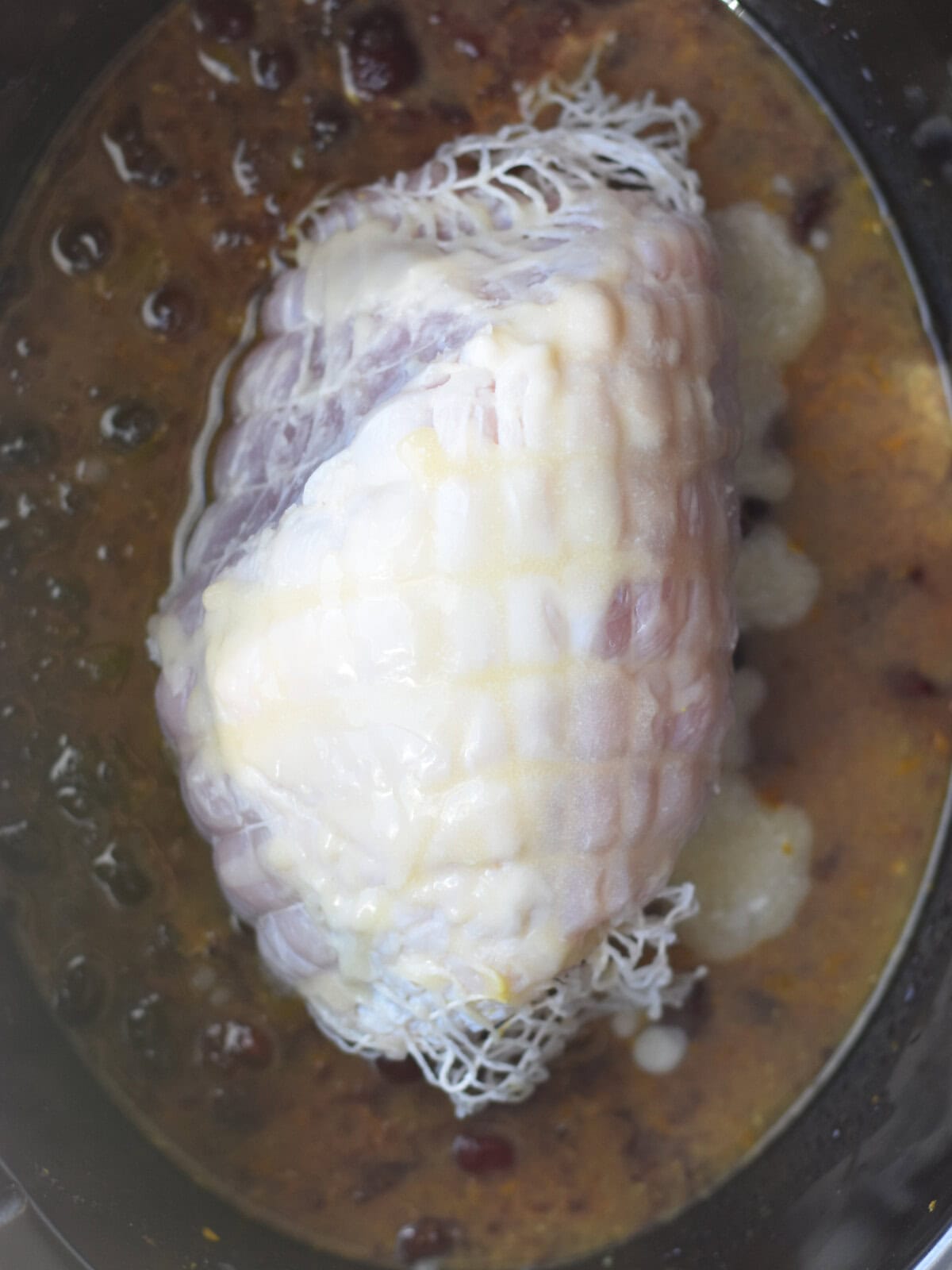 Meat in netting in a crock pot with gravy. 