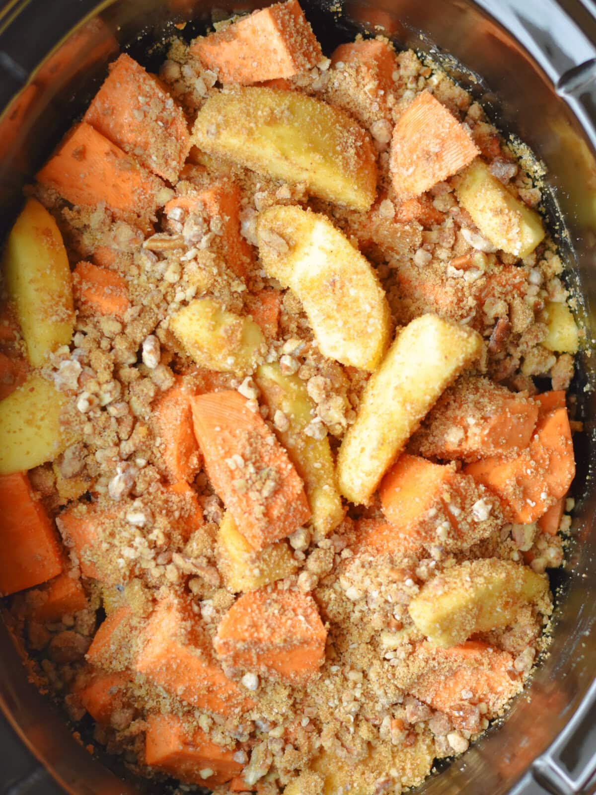 Sweet potatoes and apples with crumble topping in a slow cooker uncooked. 