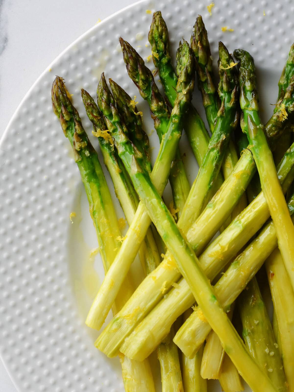 Lemon Roasted Asparagus on a white plate on a marble countertop. 