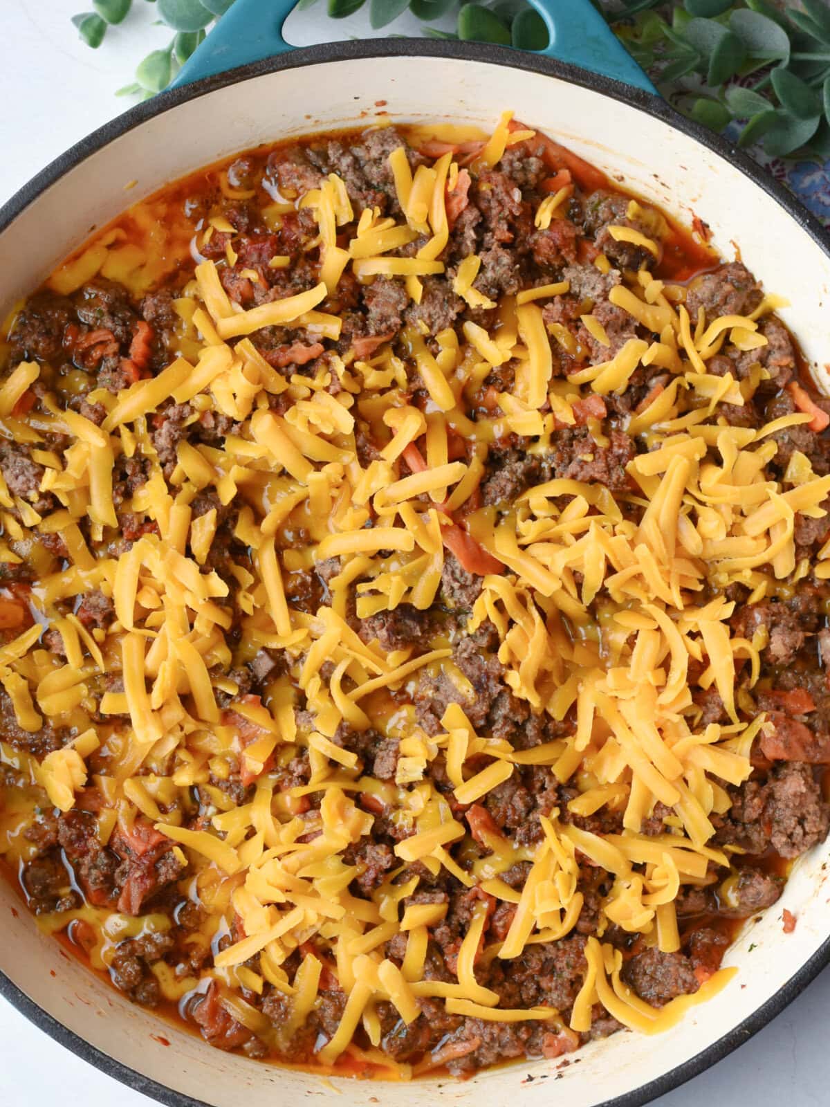 Ground beef mixture, tomato paste and shredded cheese in a skillet. 