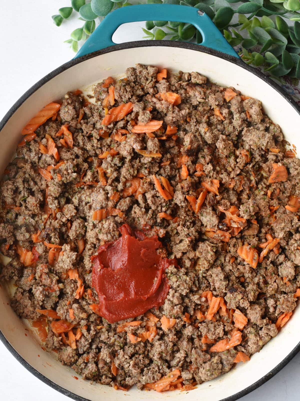 Beef mixture and tomato paste in a skillet. 