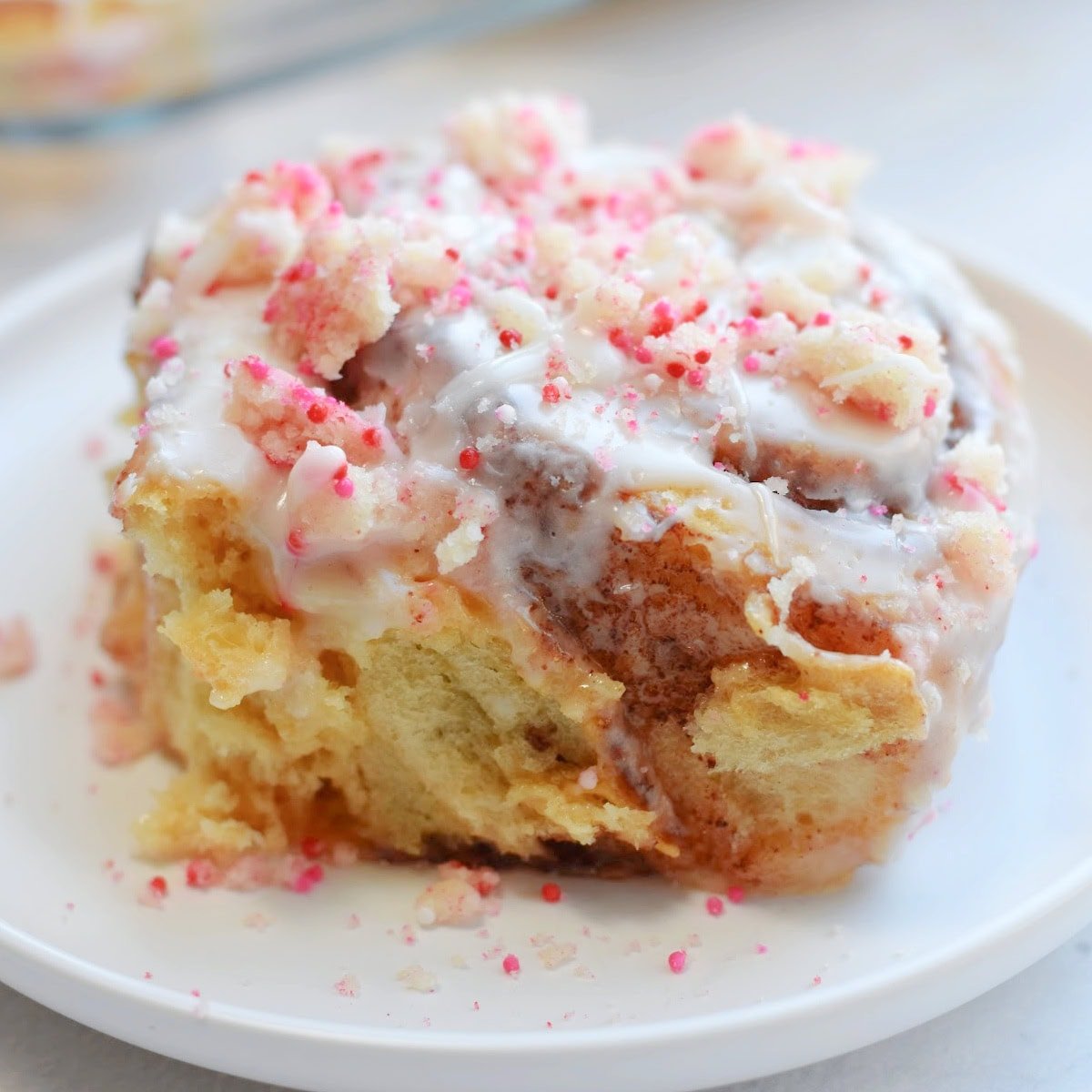 Sugar cookie cinnamon roll on a white plate with red and pink sprinkles.
