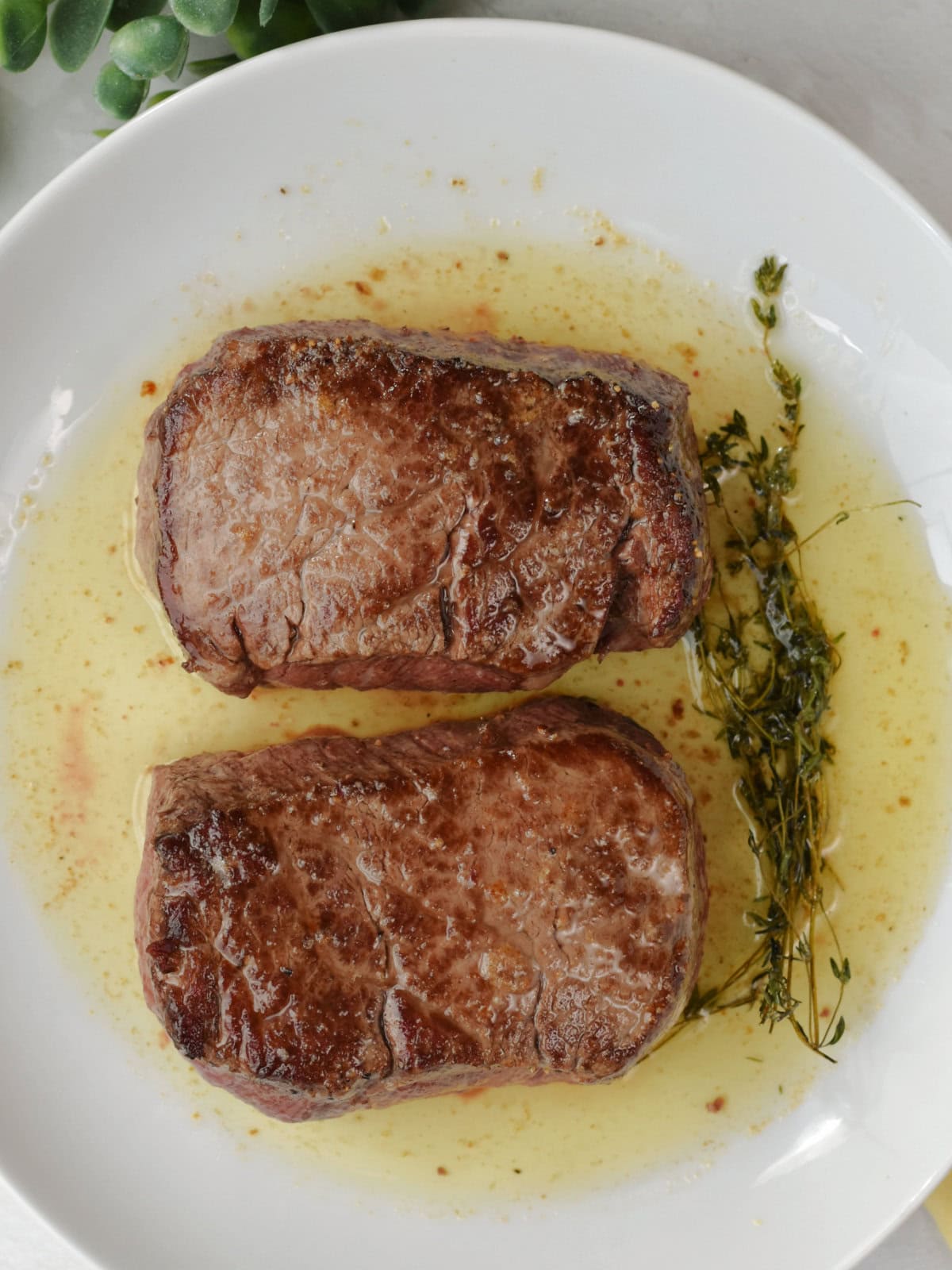 filet-mignon-oven-plate Seared and oven baked steaks with butter spooned on top of it on a white plate.