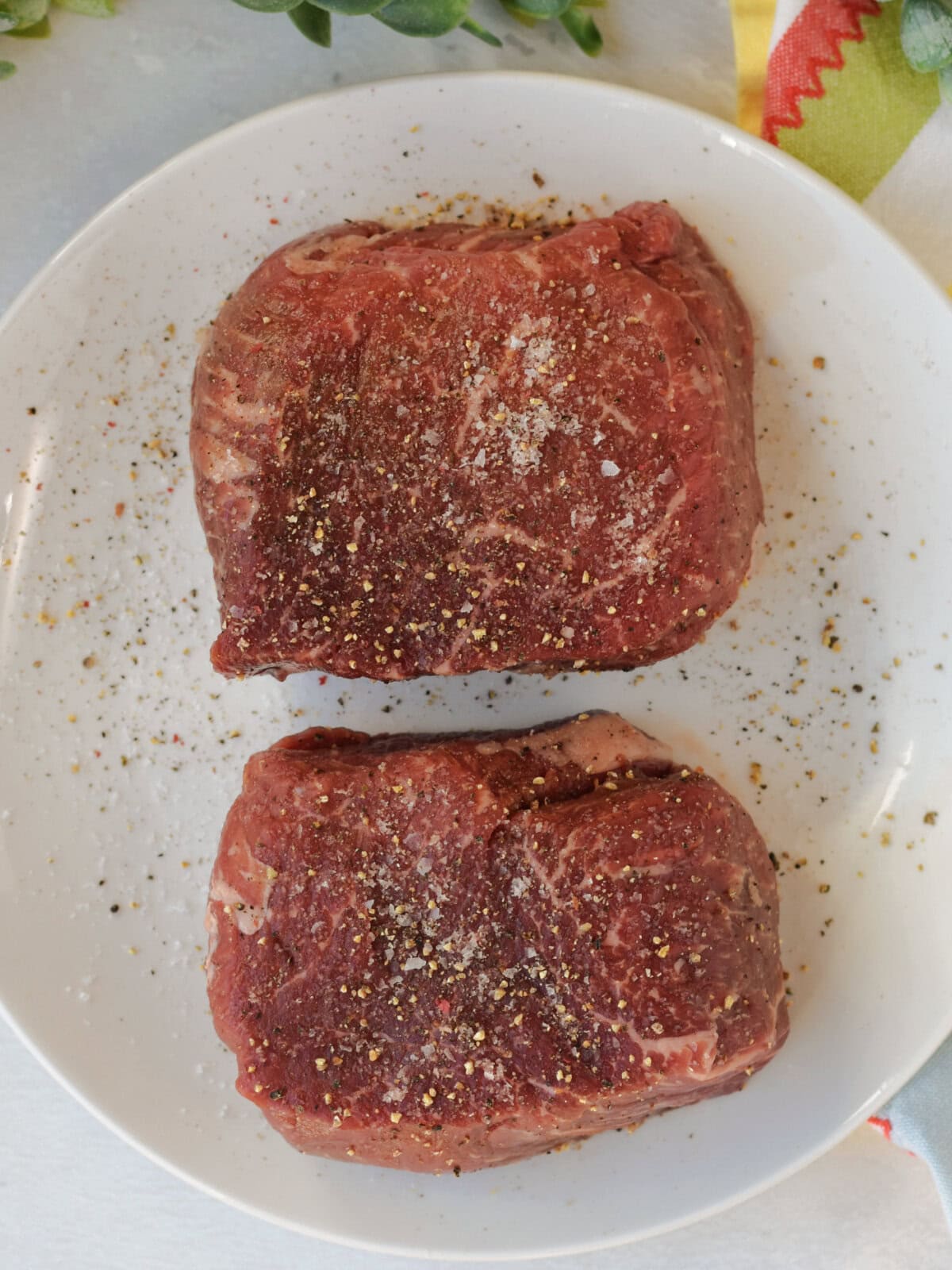 filet-mignon-oven-seasoned Two steaks seasoned with salt and pepper on a white plate.