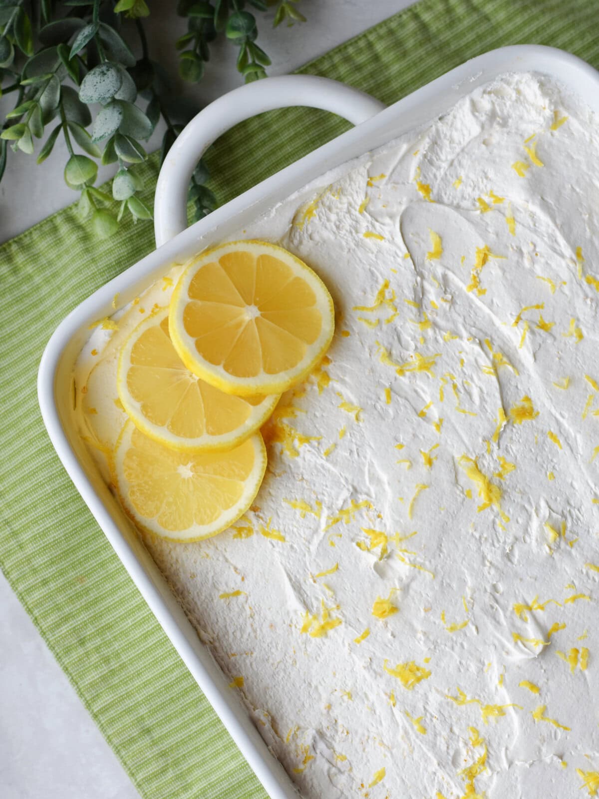 Lemon Poke Cake made in a 9X13 pan with sliced lemons and lemon zest as garnish. 