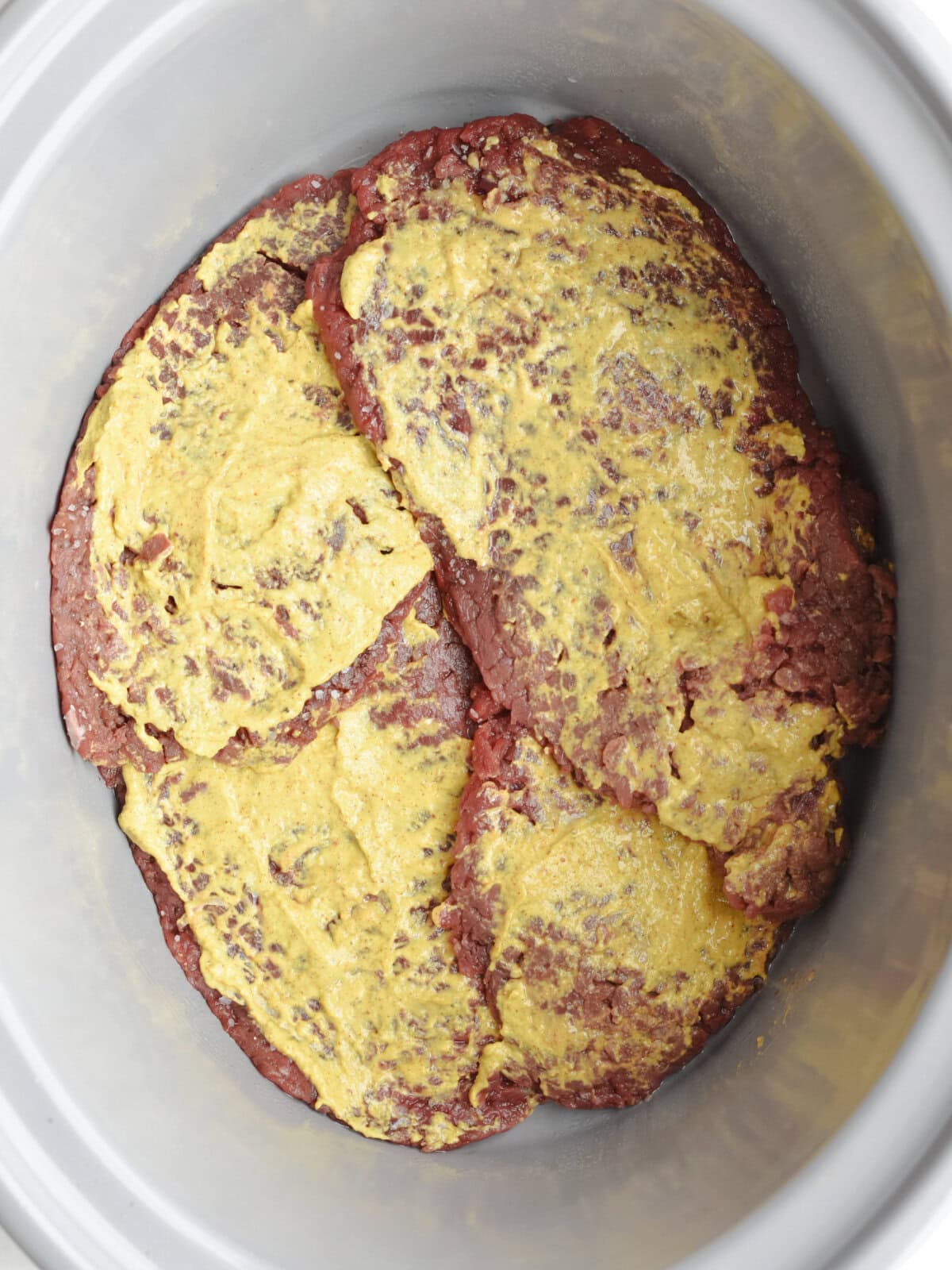 crockpot-round-steak-mustard Round steak covered with mustard in a crockpot.