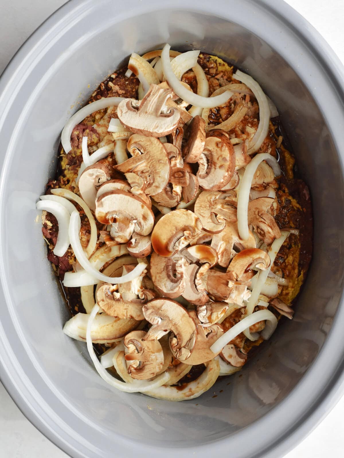 crockpot-round-steak-mushrooms Beef, cream of mushroom soup, onions, and freshly sliced mushrooms in a slow cooker.
