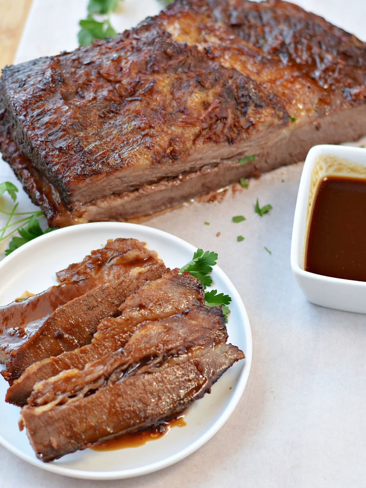 Beef brisket made in the electric roaster oven on a serving plate with bbq sauce and a the whole brisket behind it. 
