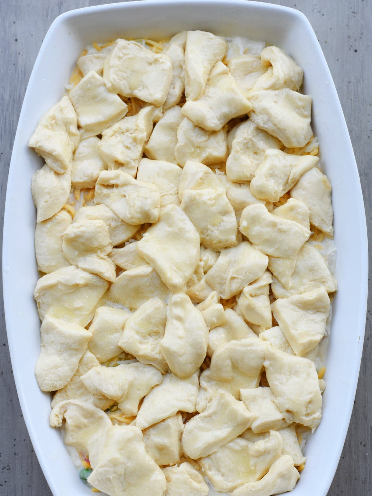 Uncooked canned biscuits layered over a casserole filling in a baking dish. 